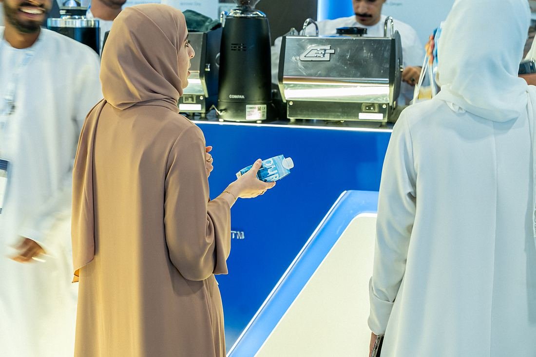 A visitor holding an OURWATER carton bottle at the stand