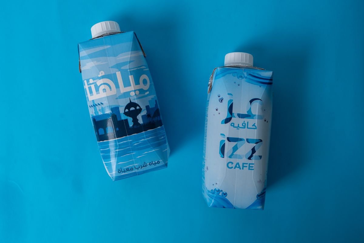 Two OURWATER cartons on a blue background: the OURWATER design and a custom IZZ Cafe design